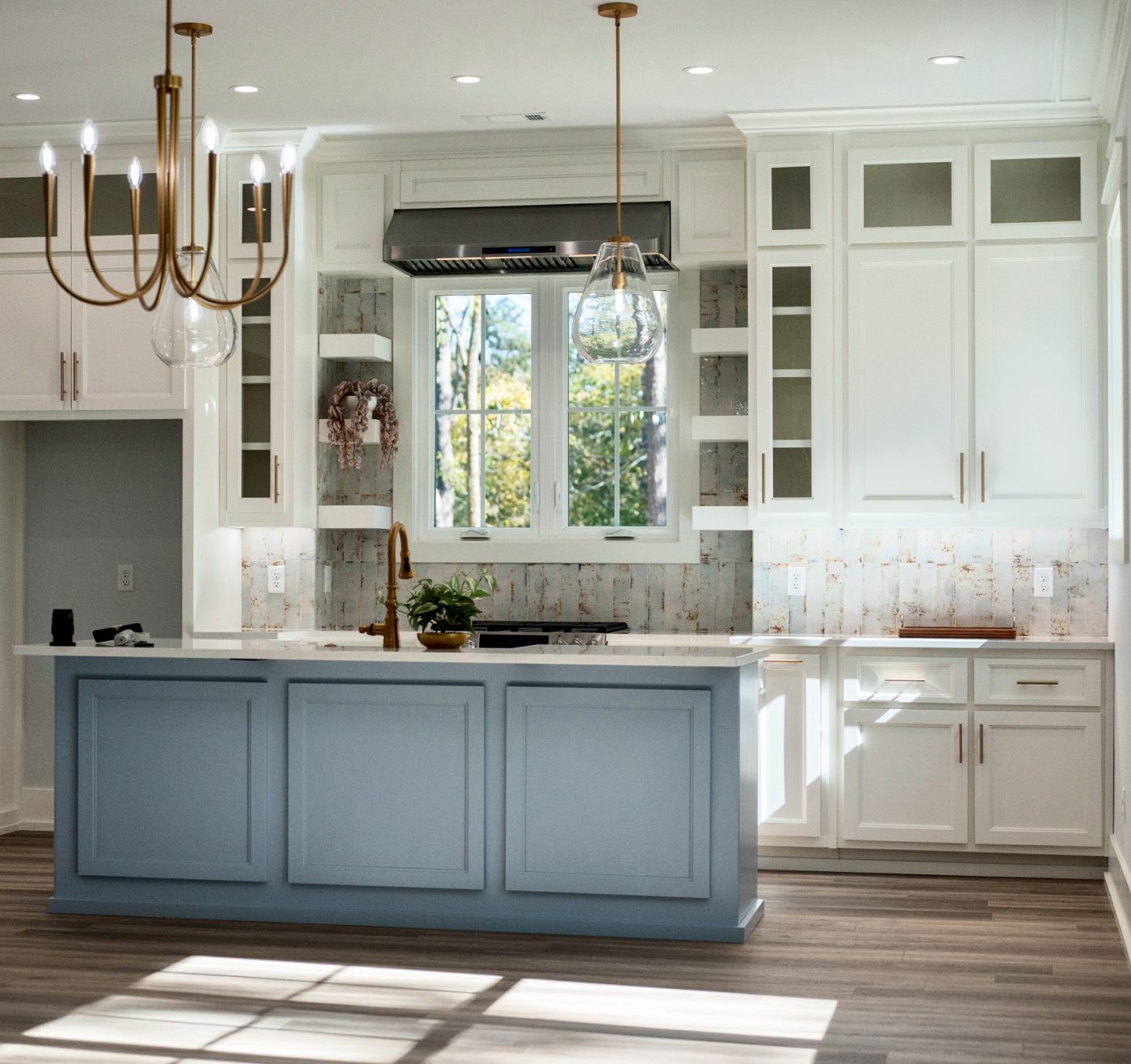 White kitchen with a blue-gray island and brass chandelier. Home designed by Brian Eicholtz.