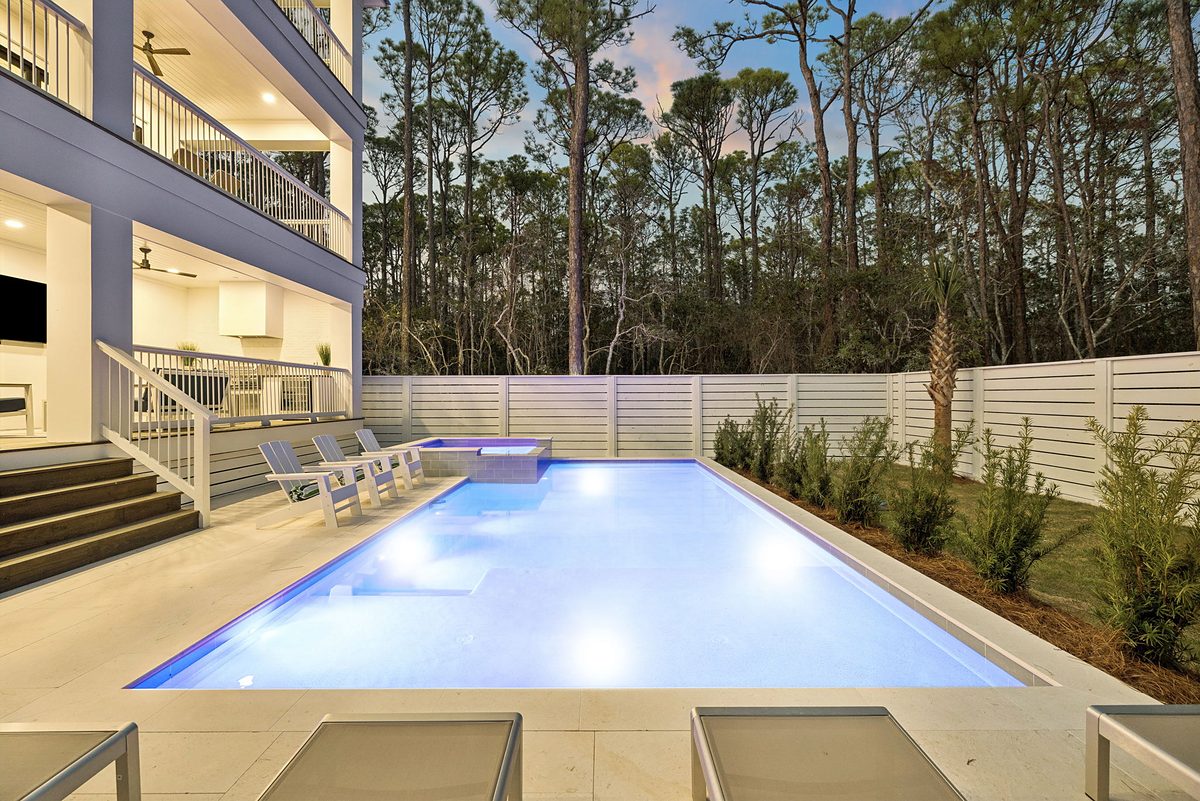 Pool and covered porches of a coastal home at dusk. Home designed by Jason Mundy.