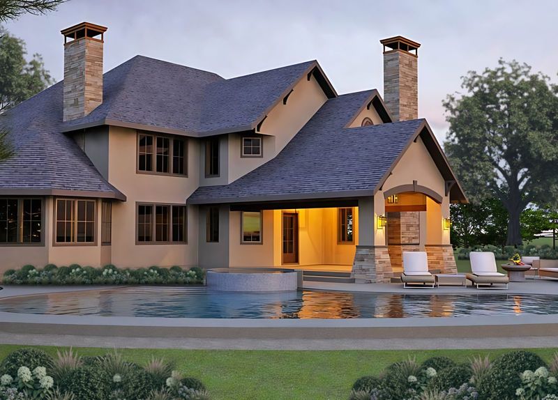 Photorealistic rendering of the rear of a stucco home at dusk with stone chimneys, a lit covered loggia, lounge chairs and a pool with a raised spa.